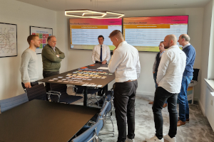Personengruppe steht um einen Tisch auf dem ein Planspiel ausliegt